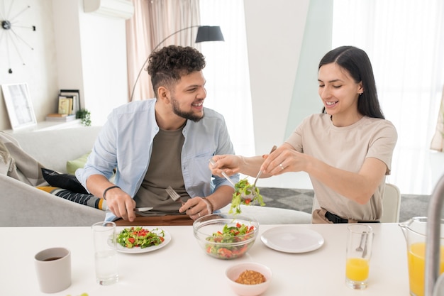 Young woman putting vegetable salad on plates during breakfast