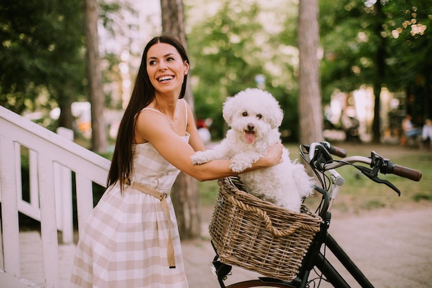 전기 자전거의 바구니에 흰색 비숑 프리제 개를 넣어 젊은 여자