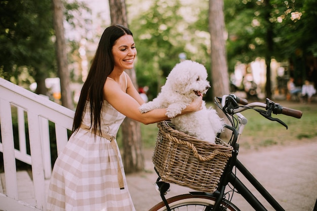 Young woman putting white bichon frise dog in the basket of electric bike