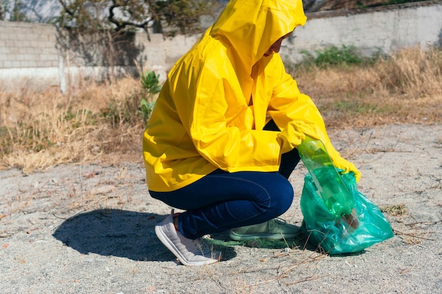 戸外でプラスチックを収集するレインコートの若い女性