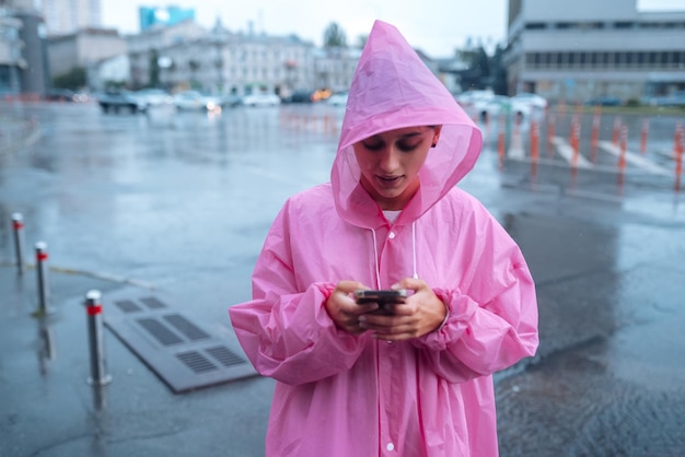 A young woman in a raincoat looking at the smartphone