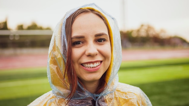 Young woman in raincoat in rainy weather Portrait of positive female in wet waterproof coat