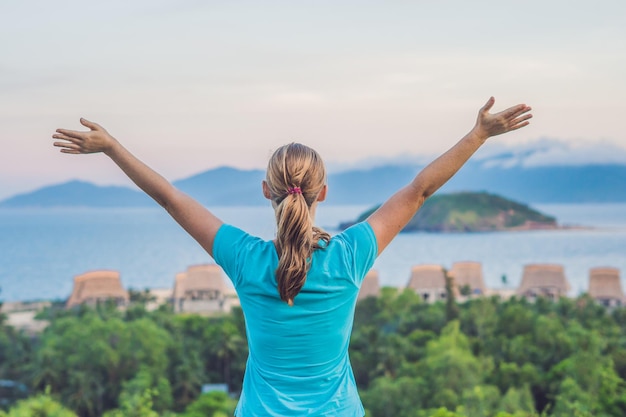 若い女性は、雲のある海、岩、空に向かって、太陽に向かって手を上げました。