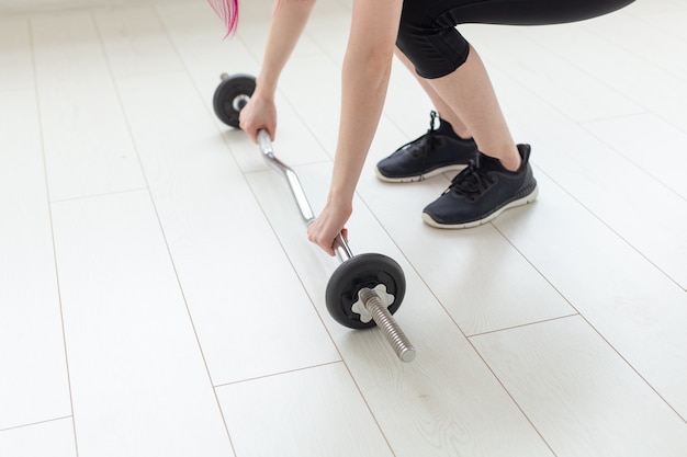 Young woman raises barbell in the spacious bright gym to perform exercises