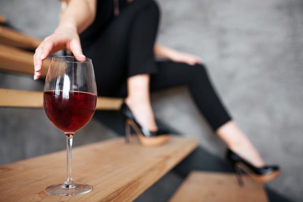 Young woman reaching hand to glass with red wine