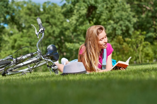 Giovane donna che legge un libro dopo aver pedalato nel parco locale