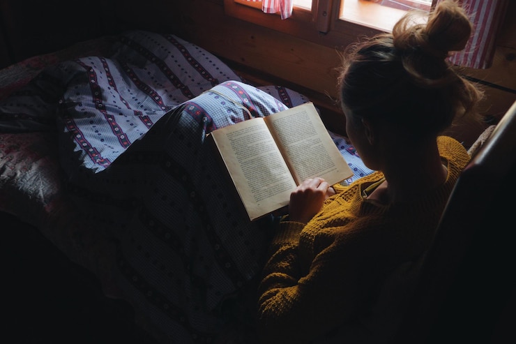 Photo 家でベッドで本を読んでいる若い女性