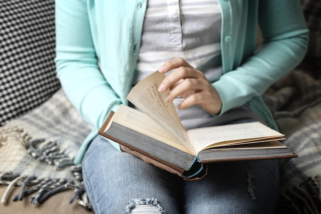 Young woman reading book closeup on home interior background