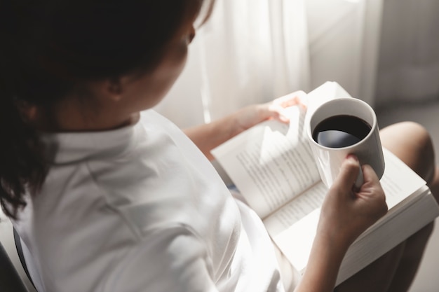 Foto giovane donna che legge un libro e che tiene tazza di caffè