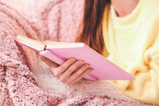 Young woman reading book at home, closeup