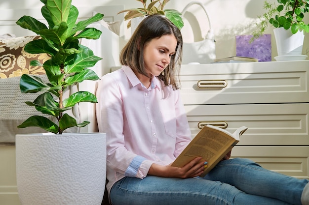 家の床に座って本を読む若い女性