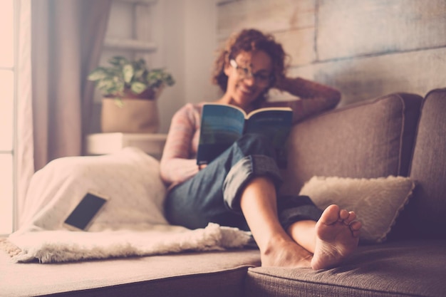若い女性が自宅のソファでリラックスしながら本を読んでいる