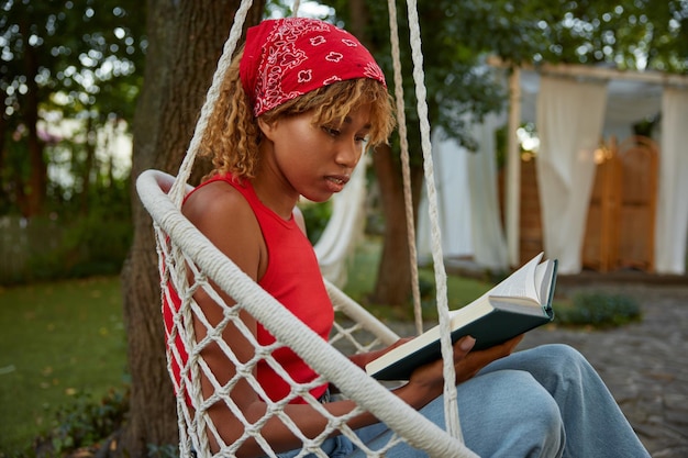 Young woman reading book while rest on hanging wicker chair