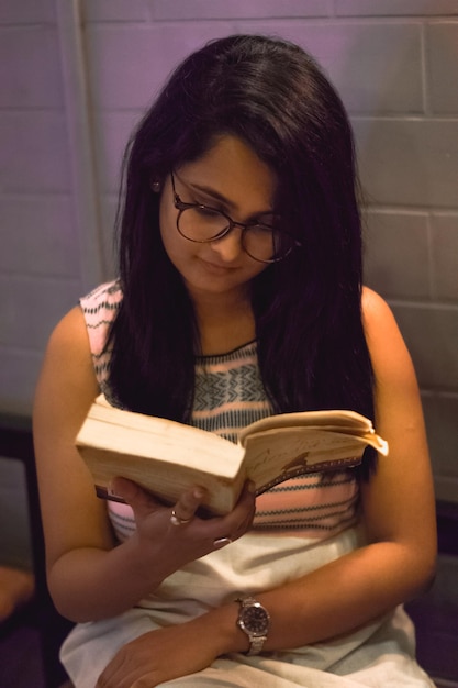 Photo young woman reading book while sitting against brick wall