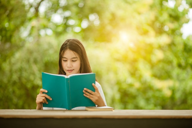 写真 公園の木に寄りかかって座って本を読んでいる若い女性