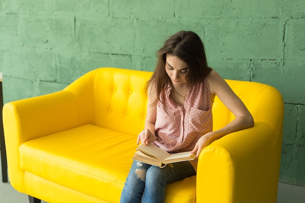 Young woman reading book on yellow sofa