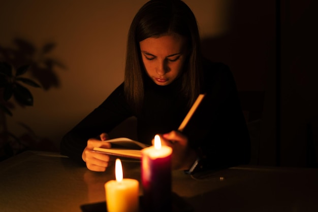 ろうそくの明かりで読んでいる若い女性。停電の概念、停電