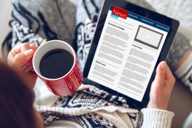 Young woman reading news using tablet while sitting on sofa at home