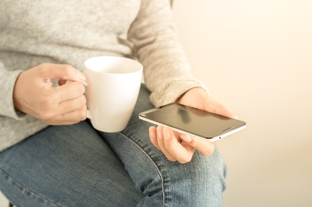 Young woman reading using phone while drinking coffee. asian caucasian woman.