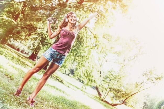 写真 若い女性は、公園で彼女のお気に入りの曲を踊り、聞いて、ヘッドフォンで現実味を帯びています。