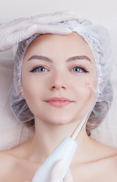 Young woman receiving electric darsonval facial massage after procedure at beauty room close up