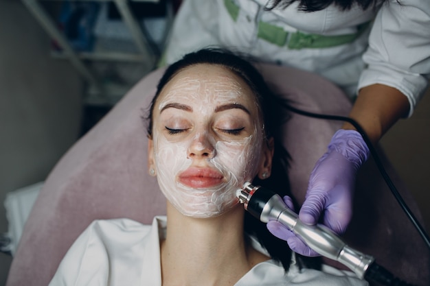 Young woman receiving electric RF lifting facial massage at beauty spa with electroporation equipment.