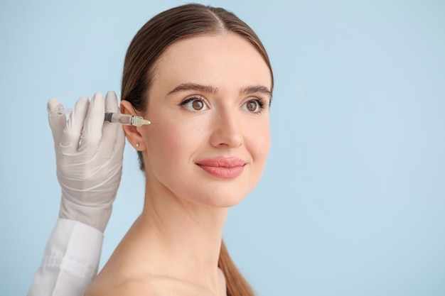 Young woman receiving filler injection against color surface