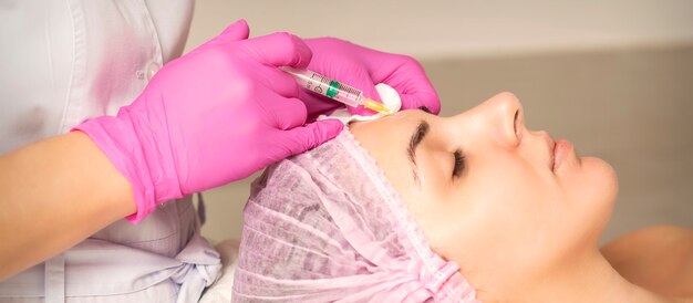 Photo young woman receiving an injection of antiaging botox filler to the forehead from a cosmetologist in a beauty salon facial treatment injection