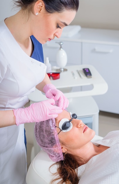 Young woman receiving laser treatment in cosmetology clinic. Eyes covered with protection glasses