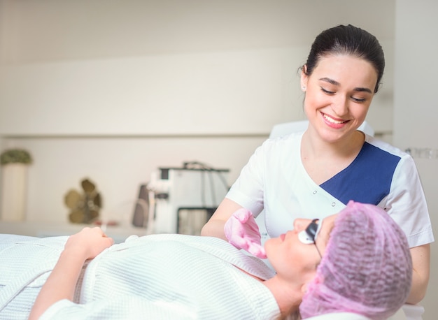 Young woman receiving laser treatment in cosmetology clinic. Eyes covered with protection glasses