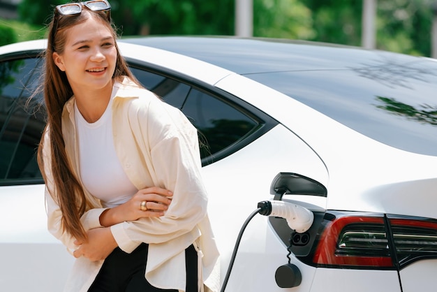 Young woman recharge her EV electric vehicle at green city park parking lot Urban sustainability lifestyle for environmental friendly EV car with battery charging station Expedient