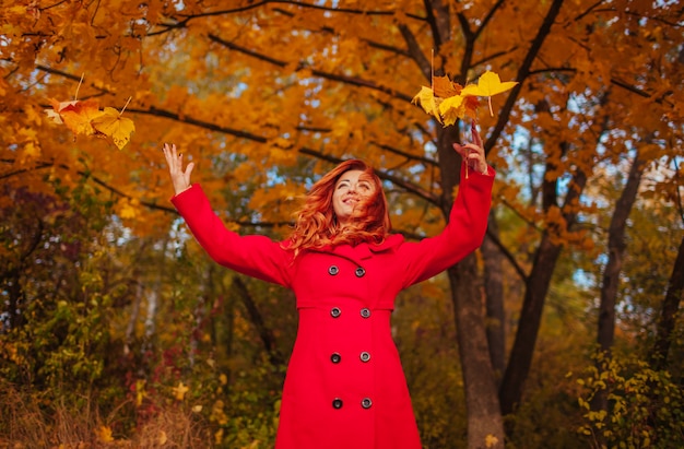 Young woman in red coat throwing leaves in the forest