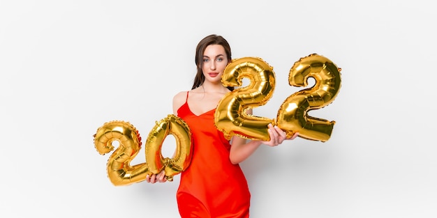 Young woman in red cocktail dress with bright makeup celebrating new year  and holding golden balloo...