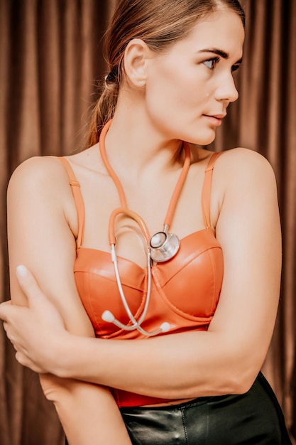 Young woman in red corset and black leather pants with a\
phonendoscope sexy brunette nurse in red