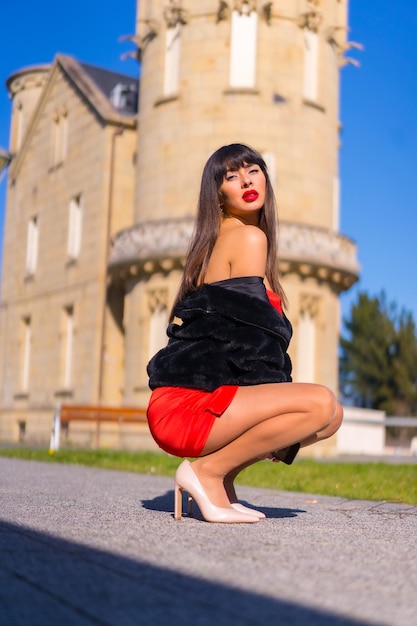 Young woman in a red dress in a beautiful castle fashionably posing and smiling in a black jacket