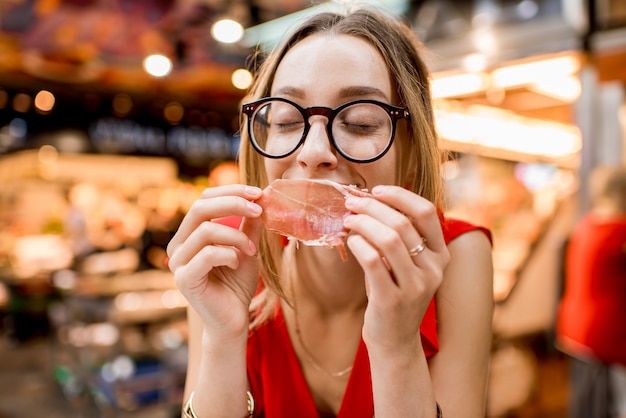 バルセロナの食品市場に座っているハモンの伝統的なスペインの生ハムを食べる赤いドレスの若い女性