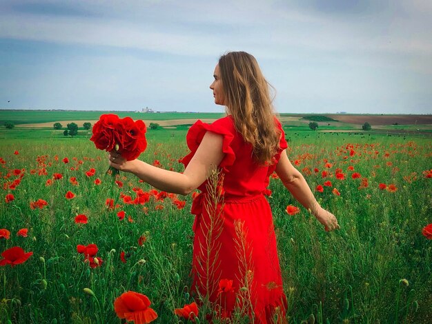 Young woman in red dress in a field of poppies