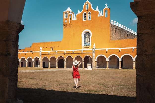 A young woman in a red dress and hat travels through the yellow city of Izamal Mexico