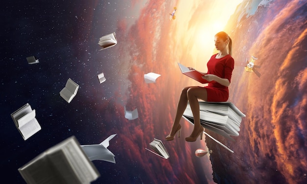 Young woman in a red dress reading a book with other books flying around. Mixed media