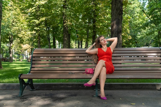 빨간 드레스에 젊은 여자 여름 공원에서 벤치에 앉아 소녀 녹색 공원 화창한 날에 달려있다