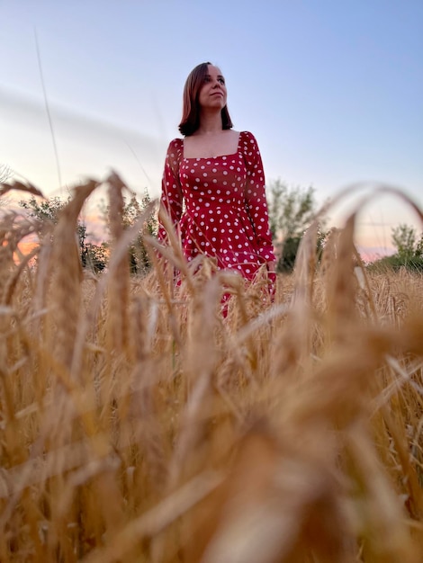 Young woman in red dress standing in wheat field at sunset