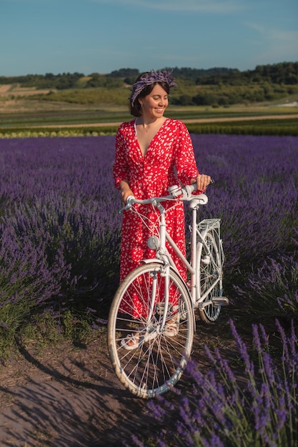 赤いドレスを着た若い女性がラベンダー畑で自転車を持って立っている