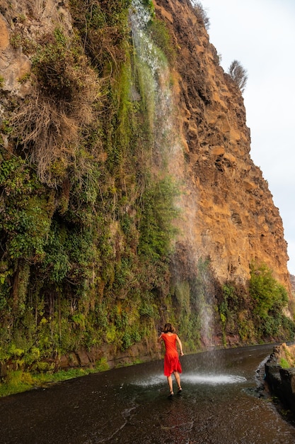 안조스 폭포 마데이라(Anjos Waterfall Madeira)라는 길에 떨어지는 폭포에서 빨간 드레스를 입은 젊은 여성