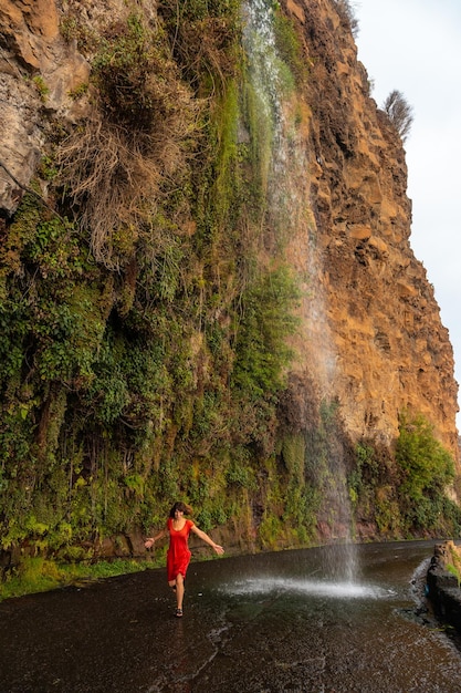 안조스 폭포 마데이라(Anjos Waterfall Madeira)라는 길에 떨어지는 폭포에서 빨간 드레스를 입은 젊은 여성