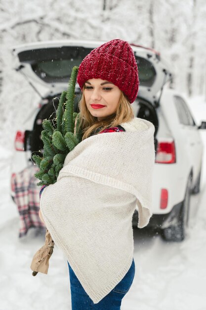 Young woman in a red hat and a white plaid with a bouquet of Christmas tree branches