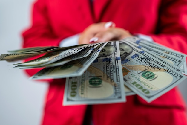 Young woman in a red jacket showing a pile of money in dollars isolated on plain background