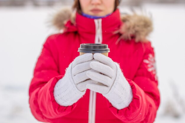 冬に赤いジャケットを着た若い女性は、ホットコーヒーまたは紅茶のグラスを保持します。