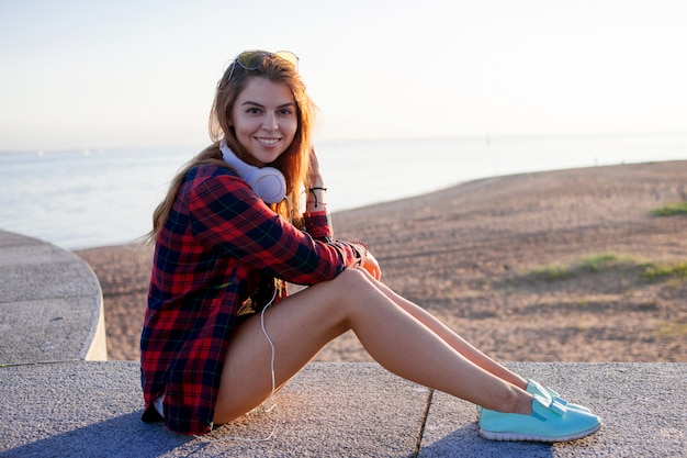 Photo young woman in a red plaid shirt with headphones, portrait outdoors