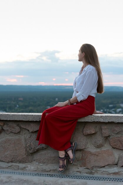 Young woman in red skirt sits on observation deck