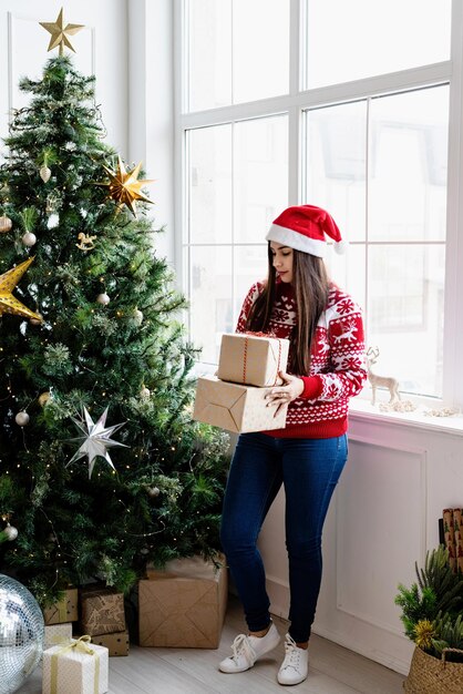 Young woman in red sweater holding a stack of christmas gifts